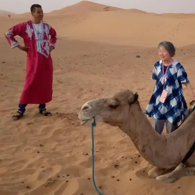 a man and a woman standing next to a camel in the desert at TRIP Merzouga luxury camp in Hassilabied