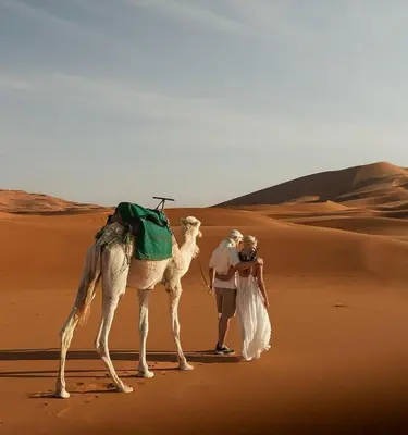 a man and woman standing next to a camel in the desert at Tranquil gem luxury camp in Merzouga