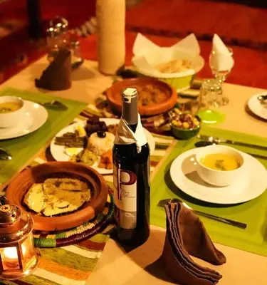 a table with a bottle of wine and plates of food at Tranquil gem luxury camp in Merzouga