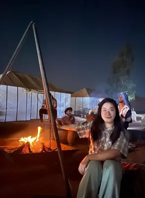 a woman sitting in front of a fire at Merzouga Paradise Luxury Camp in Merzouga