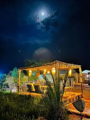 a night view of a building with the moon in the sky at Merzouga Desert Experience Camp-Erg Chebbi Sunset & Camel Ride in Merzouga