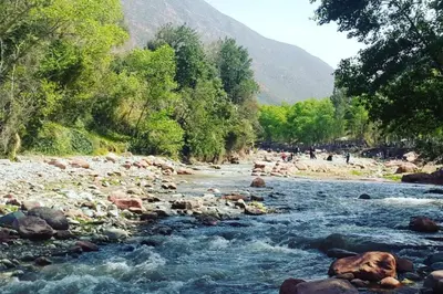a river with rocks and people walking on the shore at Dar Dahlia Atlas Valley in Oulad Akkou