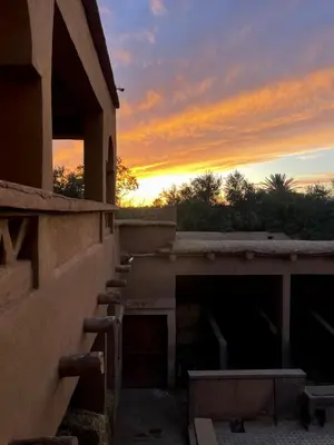 a sunset over a building with the sun setting in the background at Skoura Ranch Palm Grove in Ouarzazate