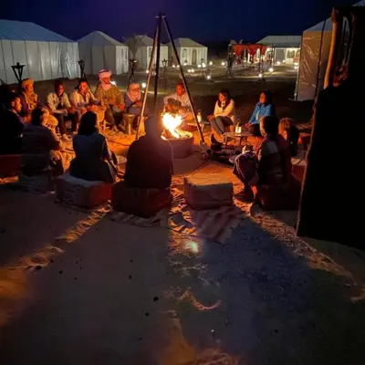 a group of people sitting around a fire at night at Merzouga tente luxury in Merzouga