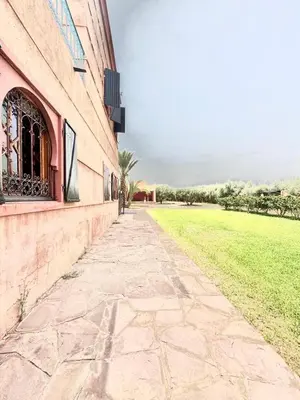 a stone sidewalk next to a building with a grass field at Villa H in Oulad Snaguia