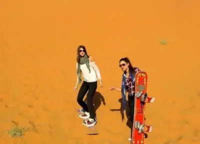 two women are riding on skateboards in the sand at Luxury Sahara Gold Camp in Merzouga