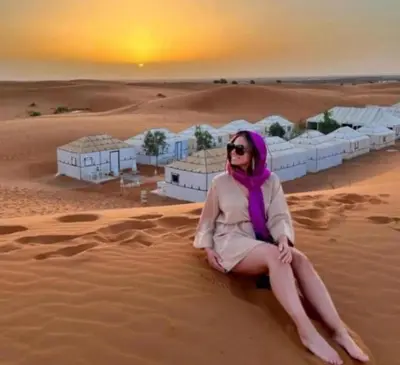 a woman sitting in the sand in the desert at Luxury Sahara Gold Camp in Merzouga