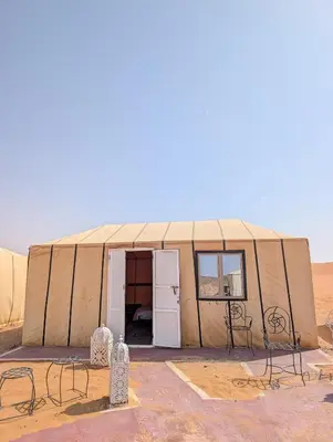 a tent in the desert with chairs and a refrigerator at Air Conditioning Berber Desert Camp in Merzouga