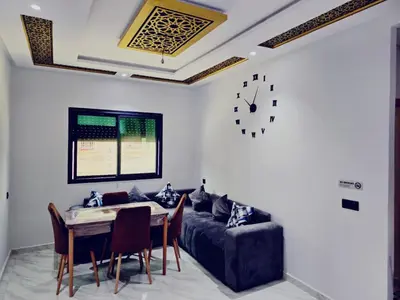a living room with a table and a couch and a clock at IM Location Euromed Fès in Fès