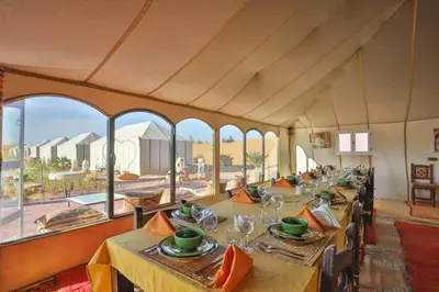 a dining room with long tables and large windows at Kabana Sahara Luxury Camp in Merzouga