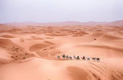 a group of people riding horses through the desert at Kabana Sahara Luxury Camp in Merzouga