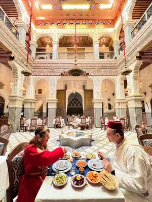 a man and a woman sitting at a table with food at Riad Fes Bab Sahra Palace in Fès