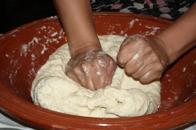 a person kneading dough in a red bowl at Riad Yamcha in Meknès