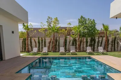 a swimming pool with chairs and a fence with palm trees at Villa Famililale Shanya in Marrakech