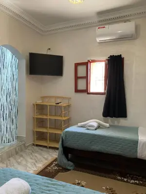 a bedroom with two beds and a television on the wall at La Belle Vue Guest House in Aït Ben Haddou