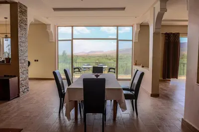 a dining room with a table and chairs and a large window at Villa Atlas View in Aghmat
