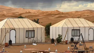 two white tents in the desert with mountains in the background at Aurora Dunes Camp in Merzouga