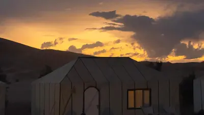 a white building with a sunset in the background at Aurora Dunes Camp in Merzouga