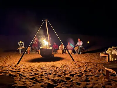 a group of people sitting around a fire on a beach at dreaming desert Luxury Camp in Hassilabied