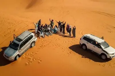 a group of people standing in the desert next to two cars at luxury desert night camp in Merzouga