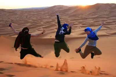 three people jumping in the sand in the desert at luxury desert night camp in Merzouga