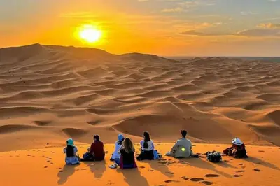 a group of people sitting in the desert watching the sunset at luxury desert night camp in Merzouga