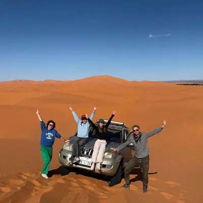 a group of people standing next to a car in the desert at Sand Fish Camp in Merzouga