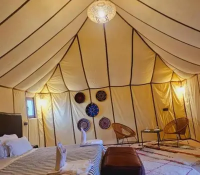 a tent with two chairs and a bed in a room at Sud Est Camp in Merzouga