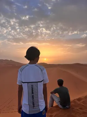 two people sitting in the desert watching the sunset at Sud Est Camp in Merzouga