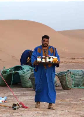 a man holding a tray of food in the desert at Starlit Desert Camp in Foum Zguid