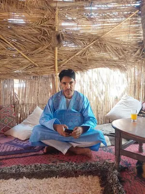 a man sitting on a bed holding a cell phone at Hassan's Guest House in Mhamid