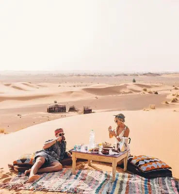 two people sitting at a table in the desert at The Desert Palace in Merzouga