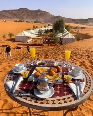 a table in the middle of a desert with food and drinks at Overnight luxury camp merzouga in Merzouga