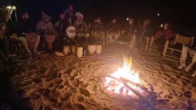 a group of people sitting around a fire in the sand at Casa caram in Hassilabied