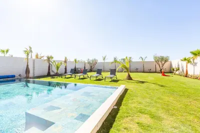 a backyard with a swimming pool and a lawn with palm trees at Villa Seyana 8 Zero Vis a Vis Piscine Chauffee in Gzoula