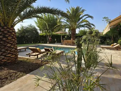 a swimming pool with benches and palm trees in a yard at Villa AIMA - avec Gourvernante in Douar Soukkane