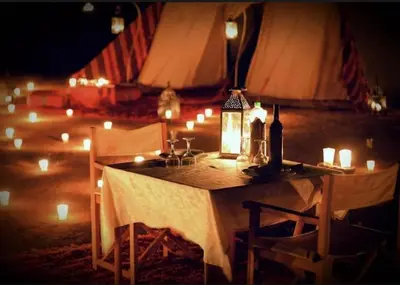 a table with candles and wine bottles on it with lights at Sandside Luxury Camp in Merzouga