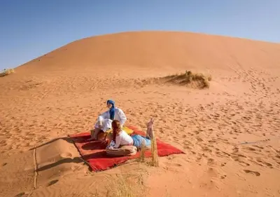 a group of people sitting on a blanket in the desert at Planet Camp Désert Tours in Mhamid