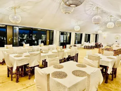 a restaurant with white tables and chairs and windows at Sahara Moon Camp in Merzouga
