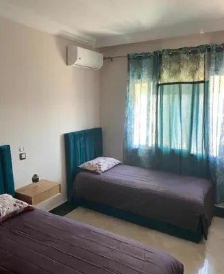 a bedroom with two beds and a window with blue curtains at Hotel ouelfa in Oulad Akkou