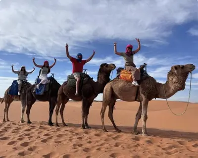 four people riding on the backs of camels in the desert at Sahara Classic Luxury Camp in Merzouga