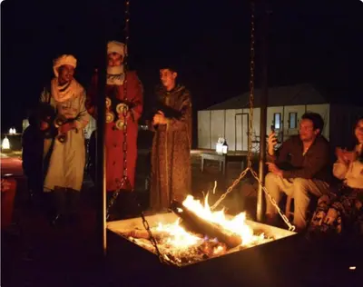 a group of people standing around a fire at Sahara Classic Luxury Camp in Merzouga
