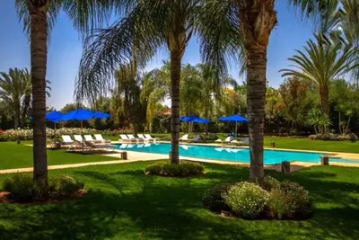 a swimming pool with palm trees and blue umbrellas at Palais pyar in Najem