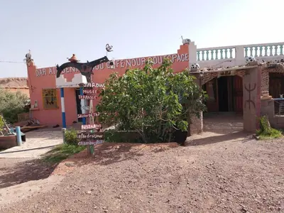 a sign in front of a building with a bush at Café nour dar ait ben haddou in Taskoukte