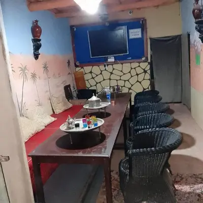 a room with a table and chairs and a tv at Café nour dar ait ben haddou in Taskoukte