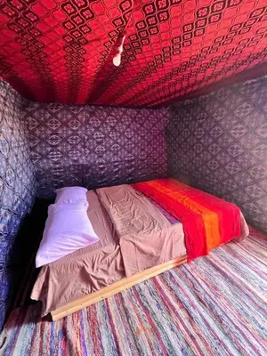a small bed with a colorful comforter in a room at Sindibad Desert Camp in Merzouga