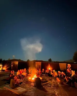 a group of people sitting around a fire at night at Sindibad Desert Camp in Merzouga