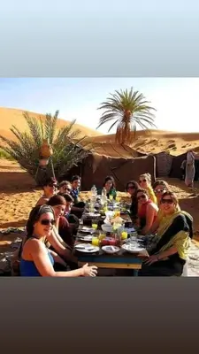 a group of people sitting around a table in the desert at Merzouga Hous in Merzouga