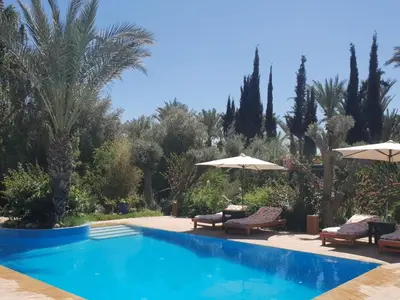 a swimming pool with chairs and umbrellas and trees at Villa palmeraie Marrakech in Najem