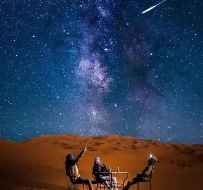 a group of three people sitting at a table under the stars at Desert Marhaba luxury Camp in Merzouga